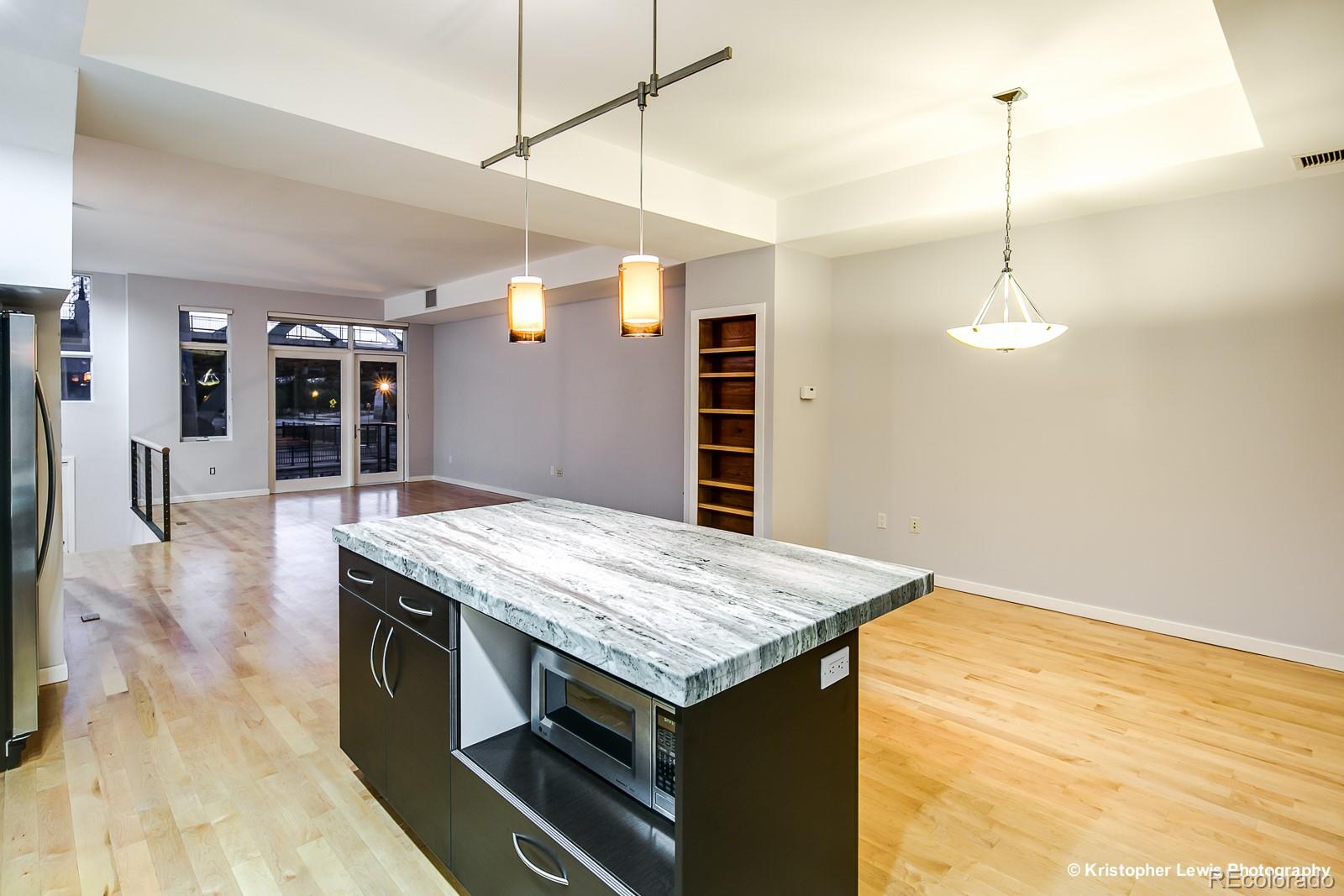 1400 Little Raven Street, Unit B Denver, CO 80202 - Photo 16 of 35 a kitchen with a stove kitchen island a refrigerator wooden floor and a view of living room