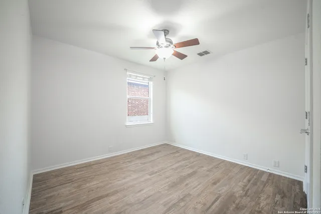 an empty room with wooden floor fan and windows