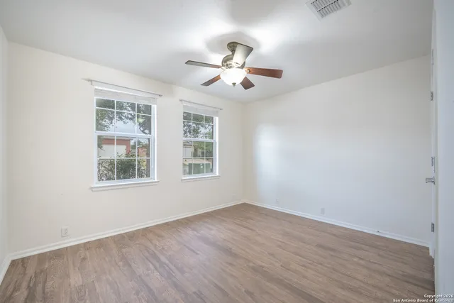 an empty room with wooden floor ceiling fan and windows