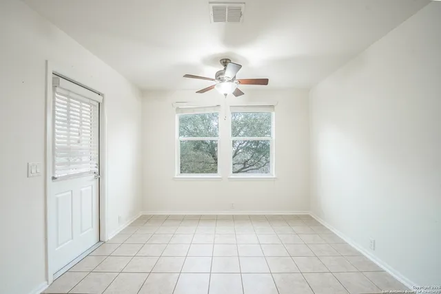 an empty room with chandelier fan and windows