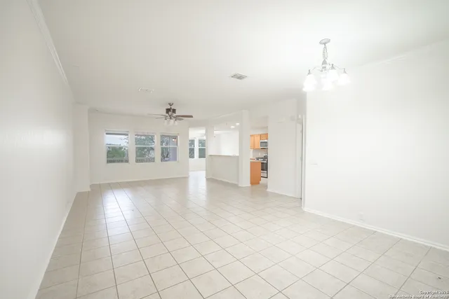 an empty room with chandelier fan and windows