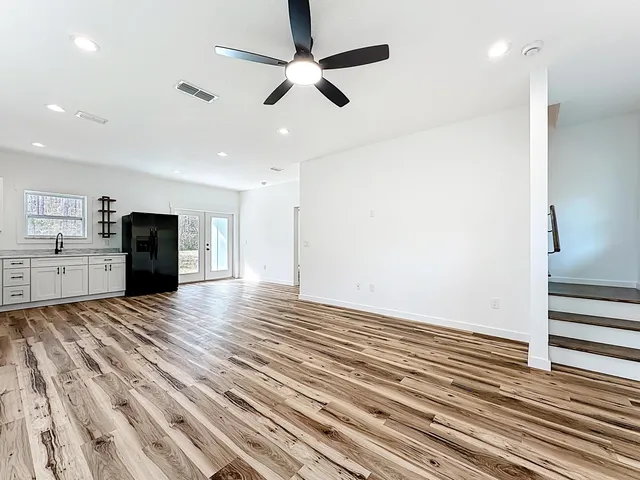 an empty room with wooden floor a ceiling fan and kitchen view