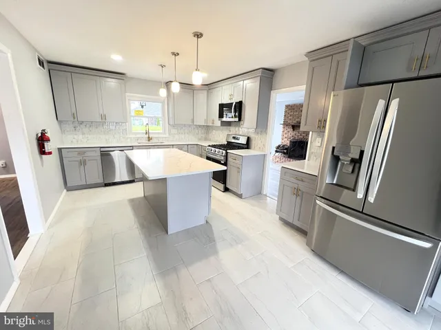 a large kitchen with stainless steel appliances kitchen island granite countertop a refrigerator a sink a stove a microwave and a refrigerator