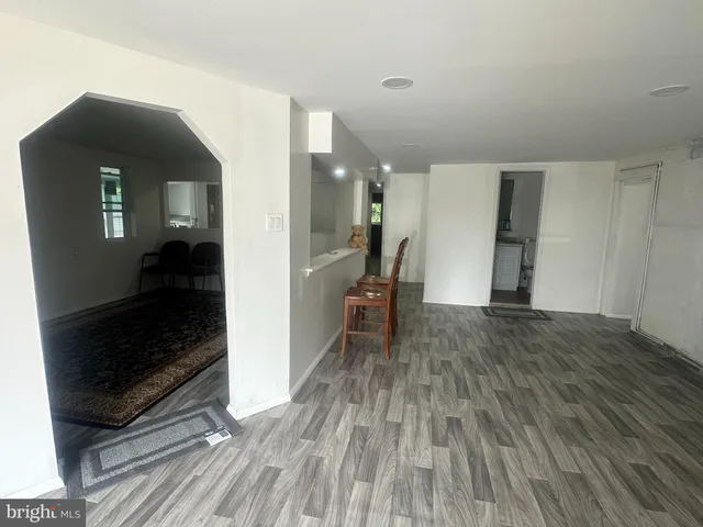 a view of a hallway to an empty room with wooden floor and a window