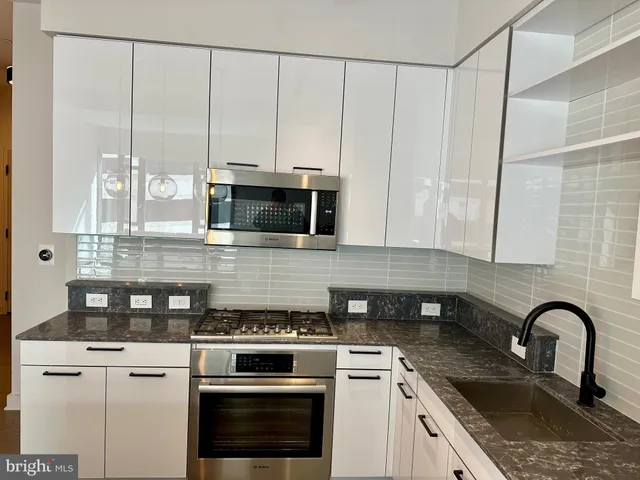 a kitchen with stainless steel appliances granite countertop a stove a sink and white cabinets