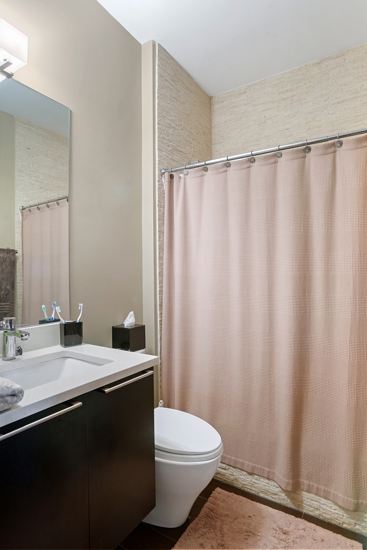 1257 West Addison Street, Unit 2 Chicago, IL 60613 - Photo 7 of 11 a bathroom with a sink a toilet a mirror and shower curtain
