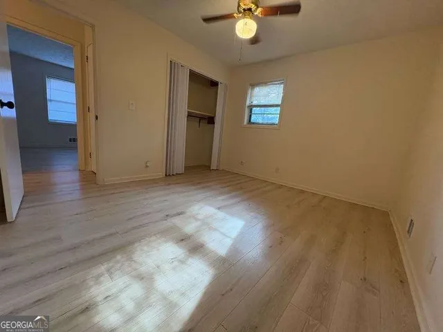 an empty room with wooden floor chandelier fan and windows