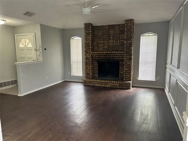 an empty room with wooden floor fireplace and windows