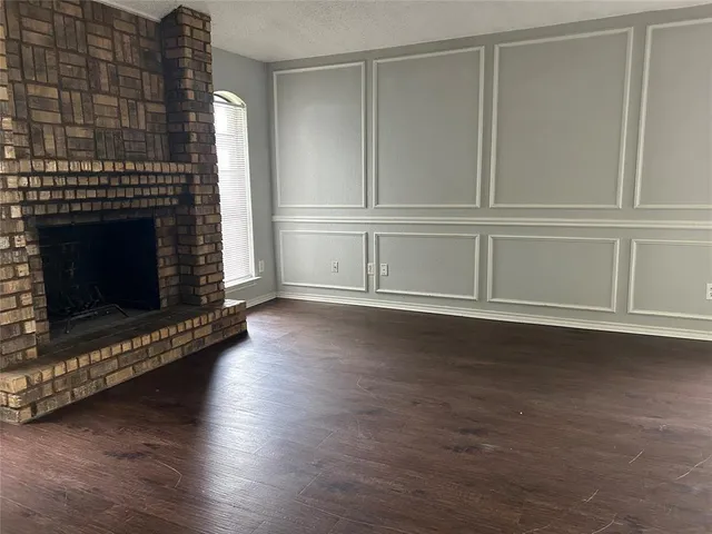 a view of an empty room with wooden floor fireplace and a window