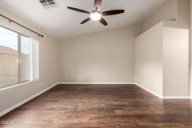 an empty room with wooden floor fan and windows