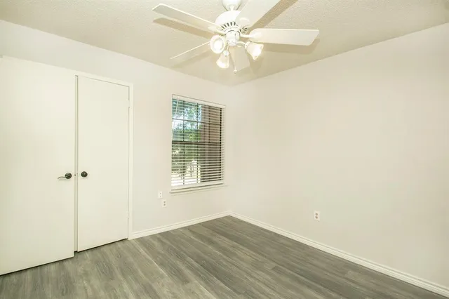 an empty room with wooden floor fan and windows