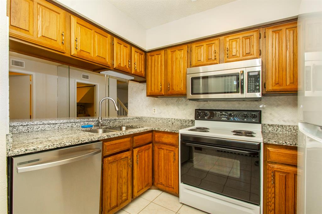 5626 Preston Oaks Road, Unit 9B Dallas, TX 75254 - Photo 4 of 20 a kitchen with granite countertop a stove microwave oven a sink and dishwasher with wooden cabinets
