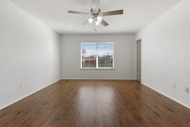 an empty room with wooden floor chandelier fan and windows