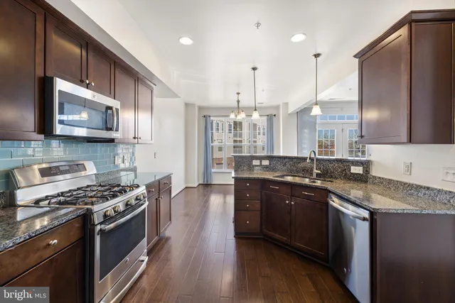 a kitchen with stainless steel appliances granite countertop a stove a sink dishwasher and a microwave with wooden floor