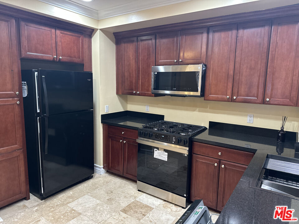 122 North Clark Drive, Unit 105 West Hollywood, CA 90048 - Photo 9 of 28 a kitchen with granite countertop wooden cabinets and stainless steel appliances