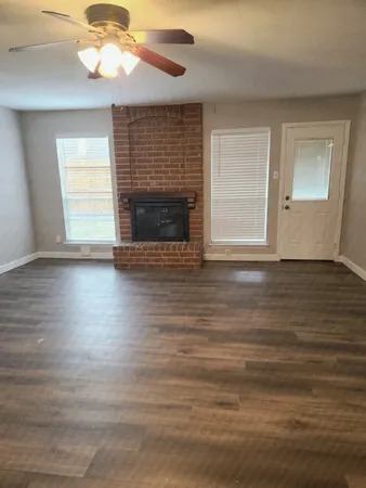 a view of an empty room with wooden floor fireplace and a window