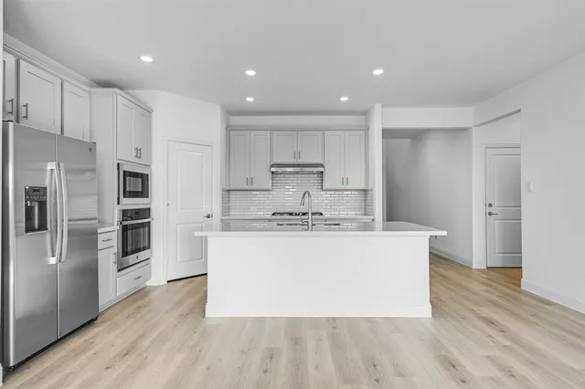 a view of kitchen with stainless steel appliances granite countertop a stove a refrigerator a sink and a microwave with wooden floor