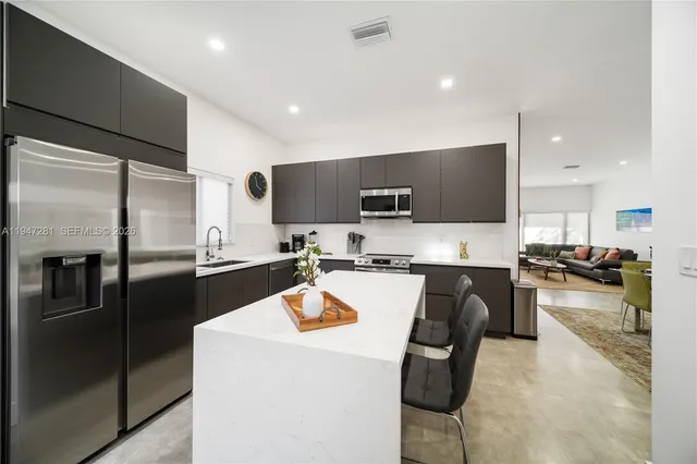 a kitchen with stainless steel appliances kitchen island granite countertop a refrigerator a stove top oven a sink with island and chairs