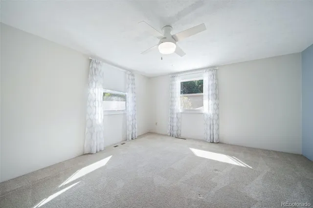 an empty room with chandelier fan and windows