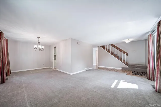a view of an empty room with stairs and a chandelier fan