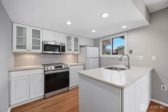 a kitchen with stainless steel appliances granite countertop a sink dishwasher a stove and a refrigerator with wooden floor