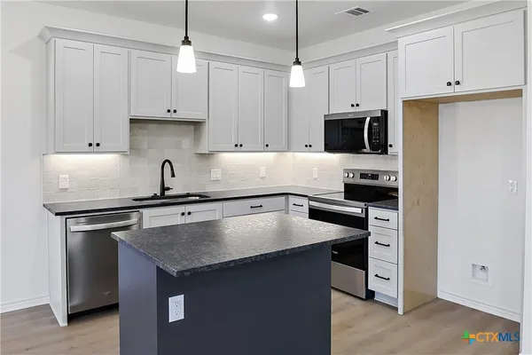 a kitchen with kitchen island a sink dishwasher and a stove with wooden floor