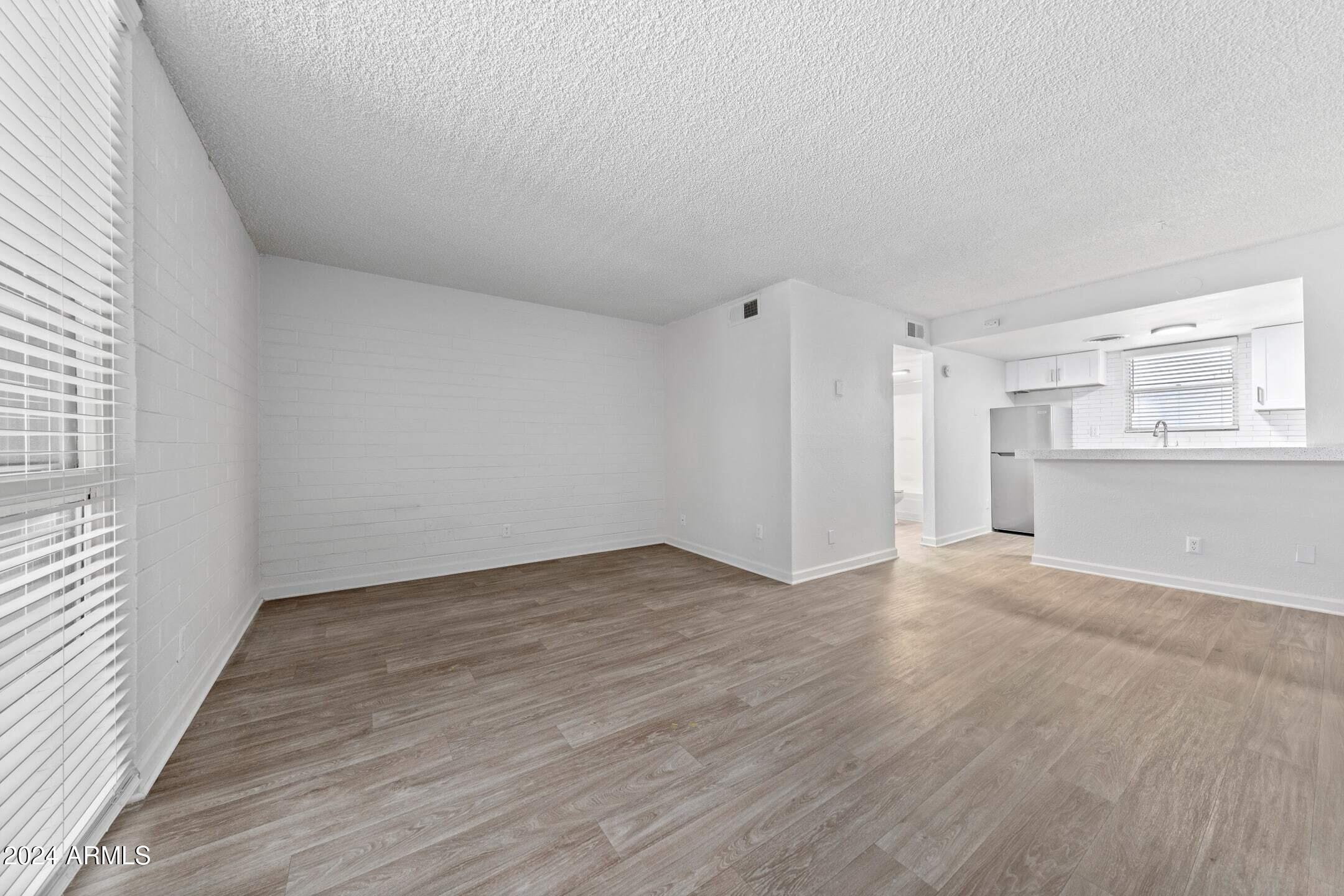 1601 West Camelback Road, Unit E10AE Phoenix, AZ 85015 - Photo 8 of 22 a view of an empty room with wooden floor kitchen view and a window