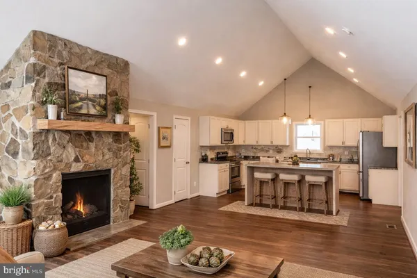 a living room with stainless steel appliances furniture a fireplace and a kitchen view