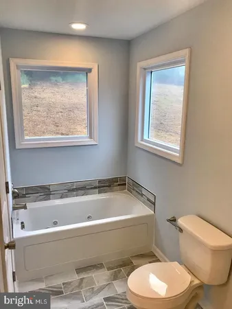 a bath tub sitting next to a white toilet and a window