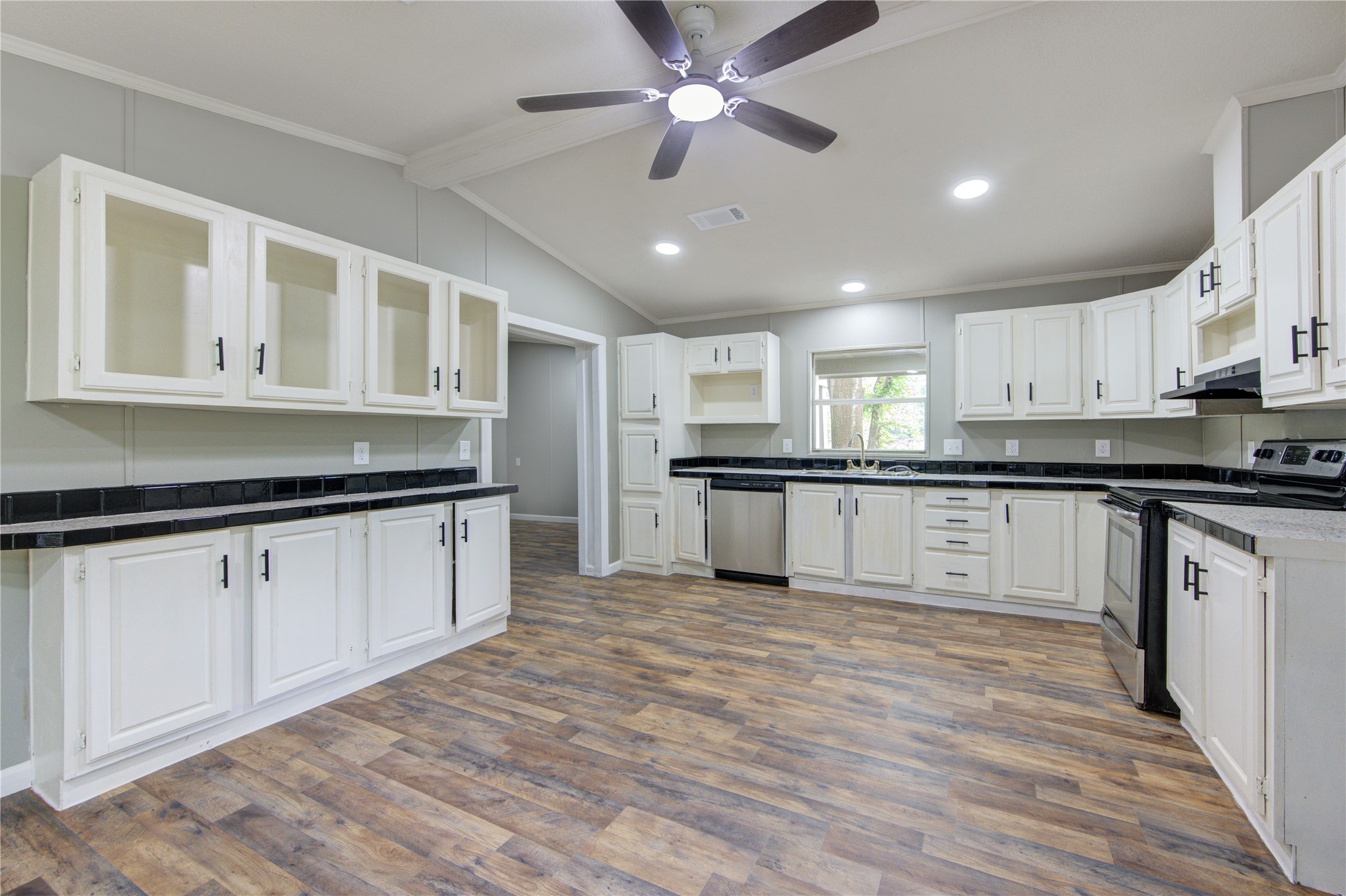 30226 Davis Street Magnolia, TX 77355 - Photo 18 of 50 This spacious kitchen features modern appliances, white cabinetry with black countertops, and wood-style flooring. A ceiling fan and recessed lighting provide comfort and brightness.