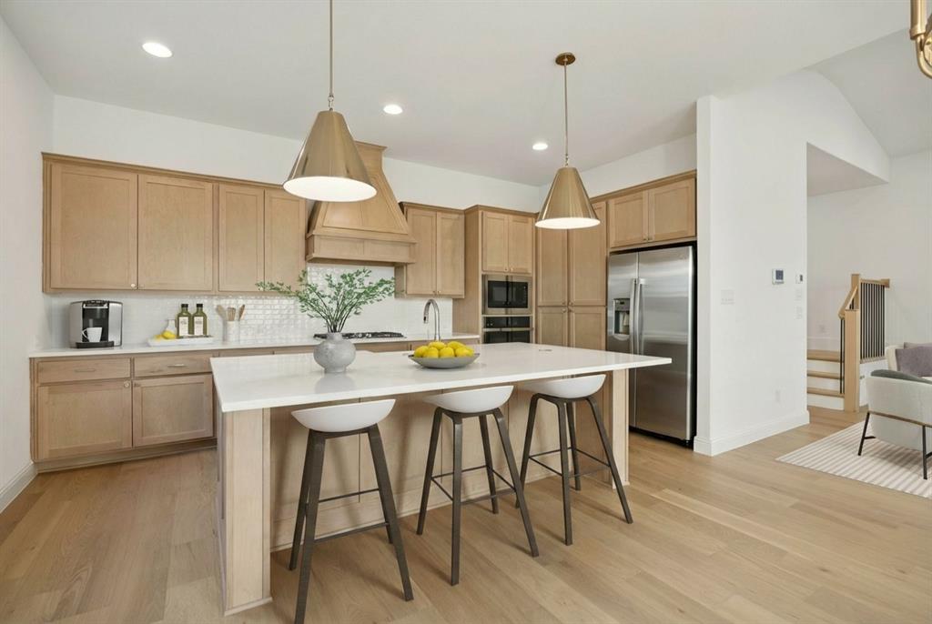 9620 Mav Lane Dallas, TX 75238 - Photo 2 of 11 Kitchen with a kitchen breakfast bar, decorative light fixtures, a kitchen island with sink, stainless steel appliances, and light wood-style floors