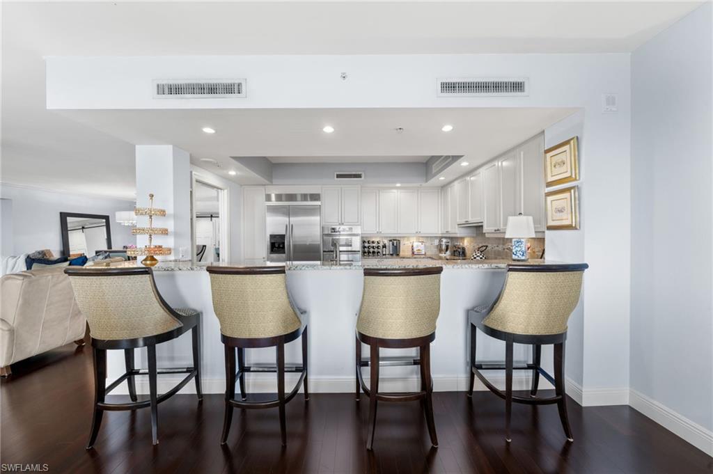 1050 Borghese Lane, Unit 902 Naples, FL 34114 - Photo 22 of 50 Kitchen with a kitchen bar, stainless steel appliances, kitchen peninsula, dark wood-type flooring, and white cabinets