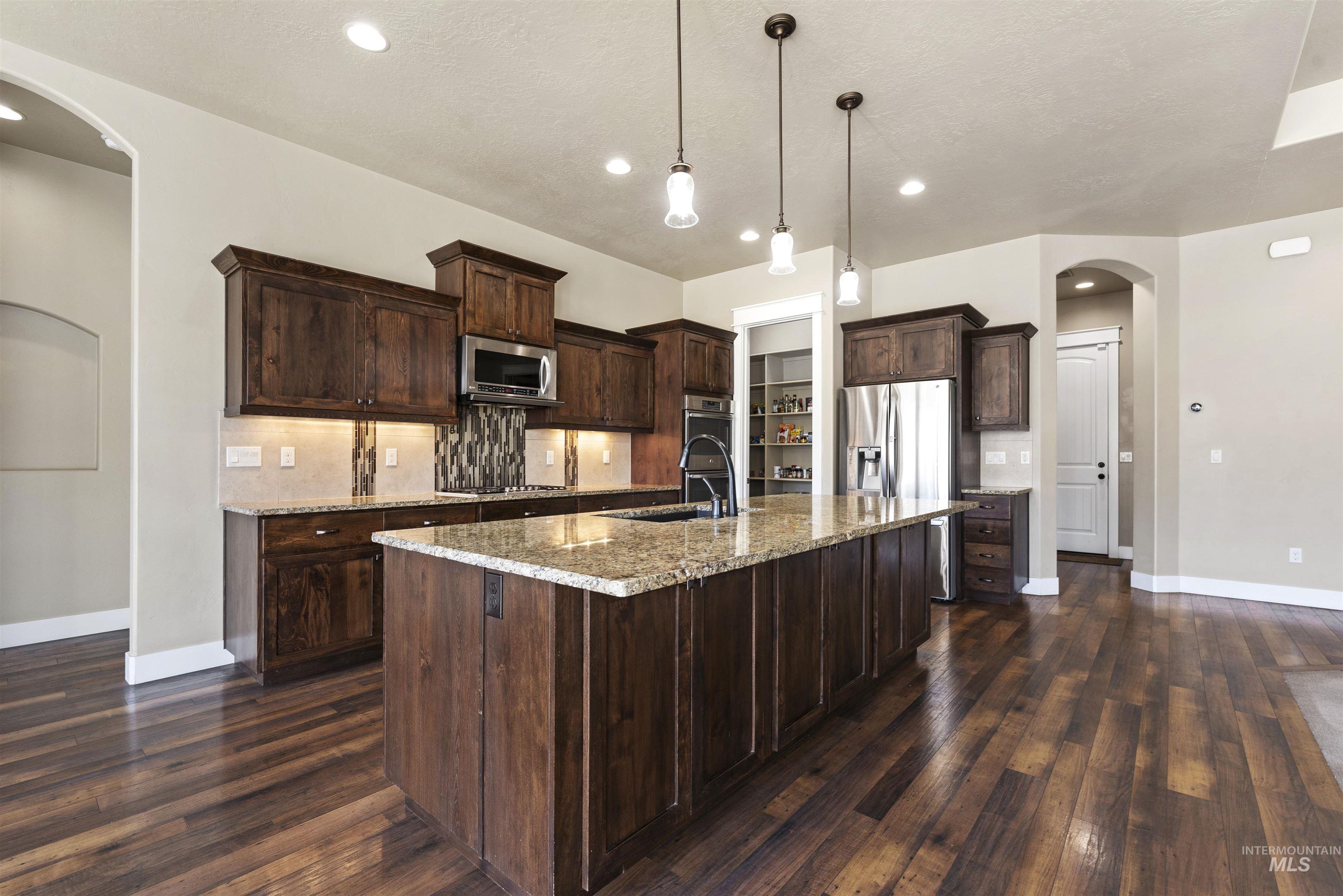 24710 Blessinger Road Star, ID 83669 - Photo 12 of 46 Kitchen featuring arched walkways, tasteful backsplash, light stone countertops, pendant lighting, and a center island with sink