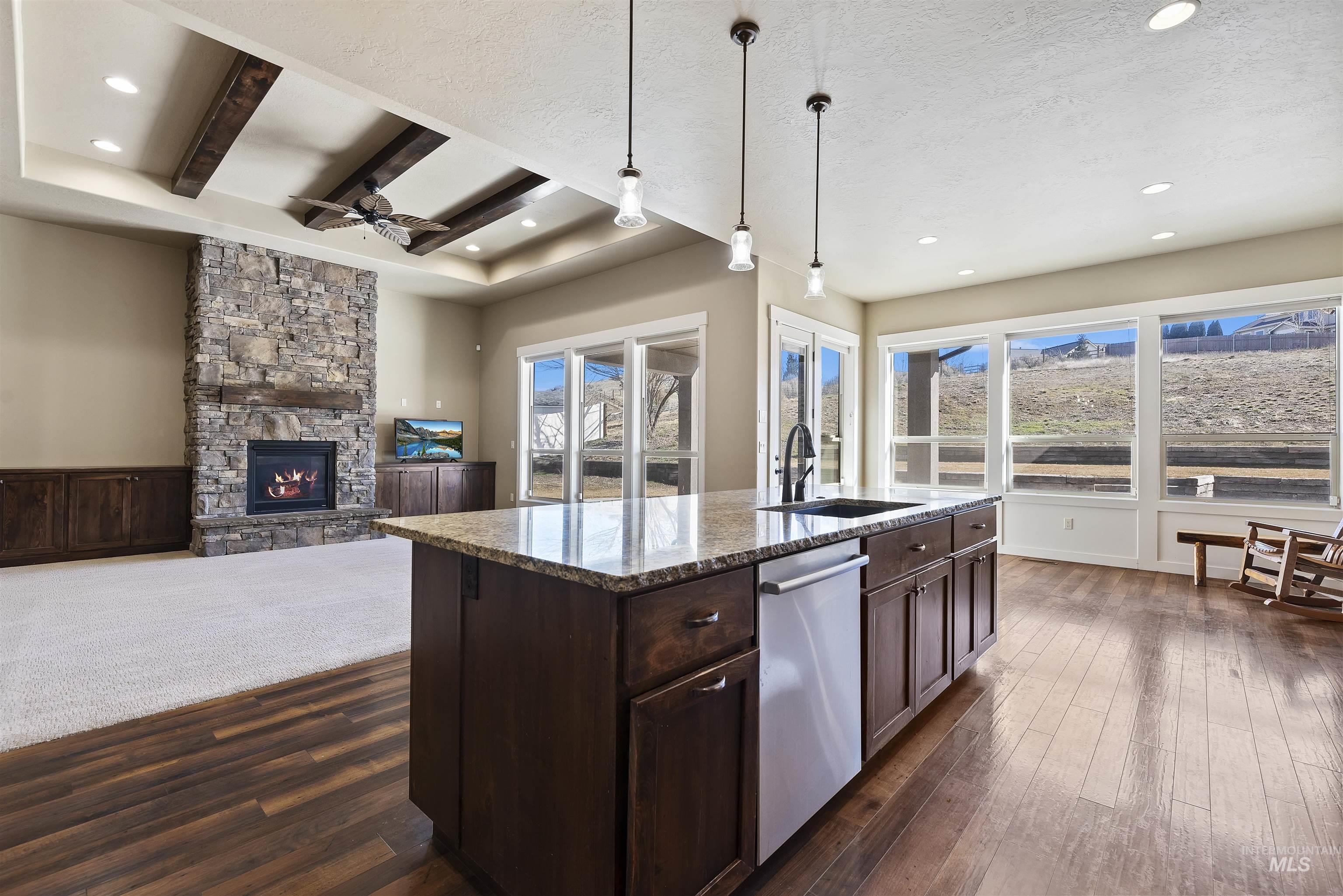 24710 Blessinger Road Star, ID 83669 - Photo 46 of 46 Kitchen featuring dark wood finish cabinetry, dark stone countertops, pendant lighting, open floor plan, and a stone fireplace