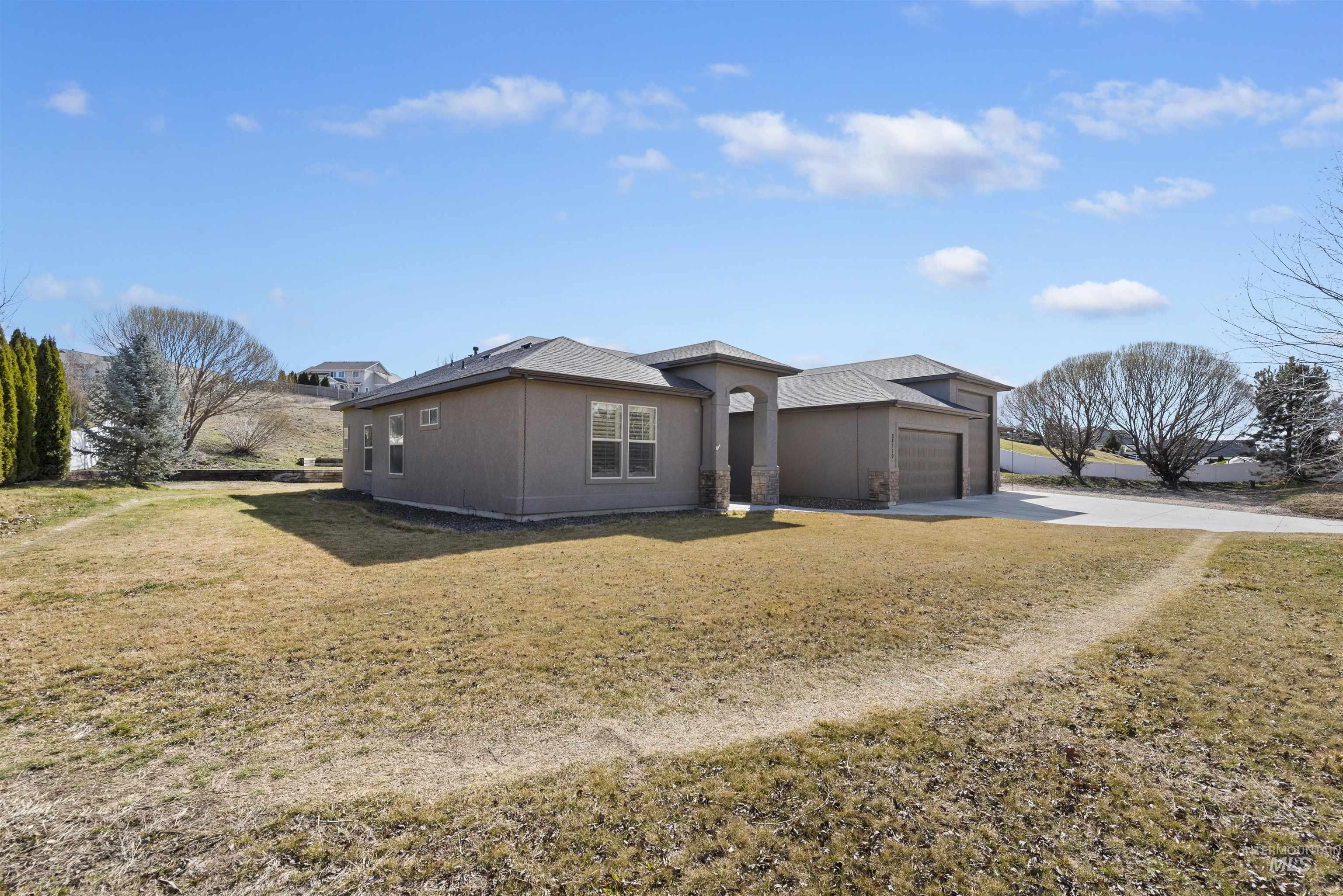 24710 Blessinger Road Star, ID 83669 - Photo 33 of 46 View of property exterior featuring a yard, driveway, stucco siding, and an attached garage