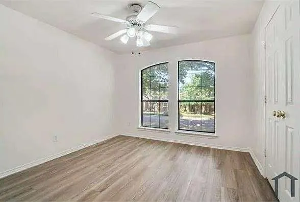 an empty room with wooden floor fan and windows