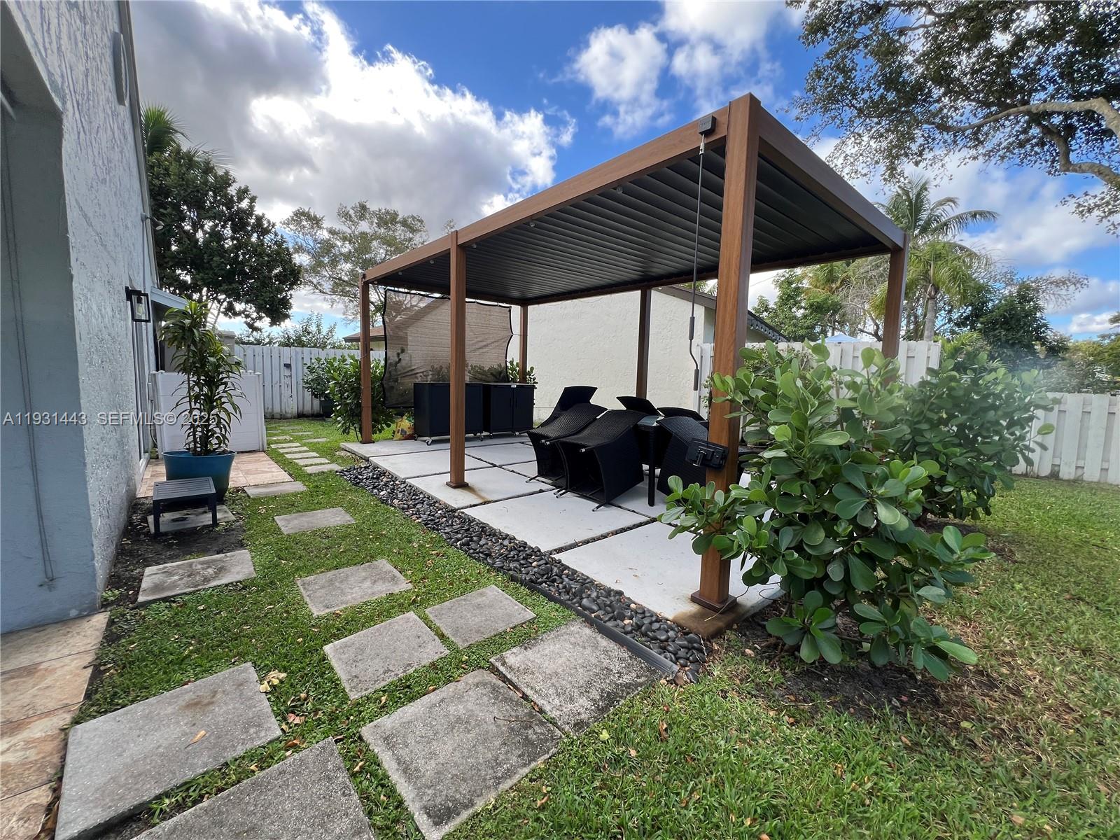 13721 Newport Manor Davie, FL 33325 - Photo 10 of 16 a view of a backyard with table and chairs potted plants and a large tree