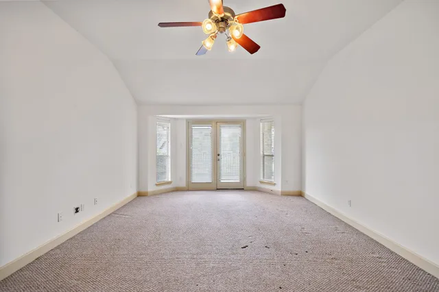 an empty room with chandelier fan and windows