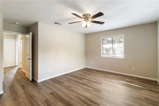 an empty room with wooden floor fan and windows