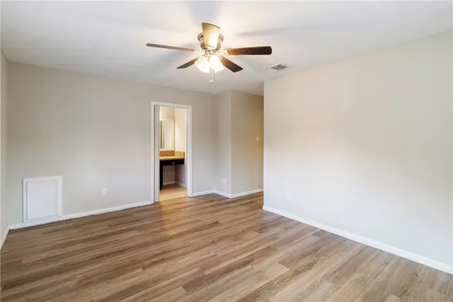 a view of an empty room with wooden floor and a ceiling fan