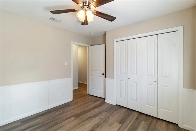 an empty room with wooden floor closet fan and windows
