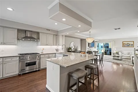 a open kitchen with stainless steel appliances granite countertop a stove top oven a sink a dining table and chairs with wooden floor