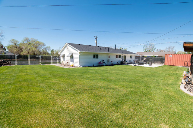 340 West 100 N Street Beaver, UT 84713 - Photo 30 of 37 Expansive backyard featuring a large green lawn, a concrete patio, a privacy fence, and a white-sided exterior with a dark shingle roof