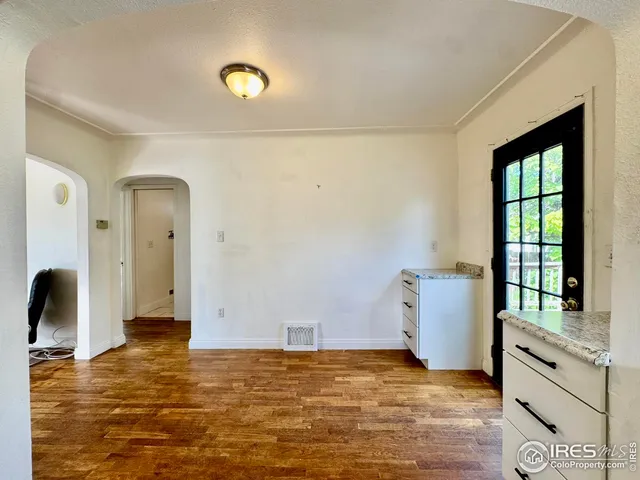 a view of an empty room with window and hardwood floor
