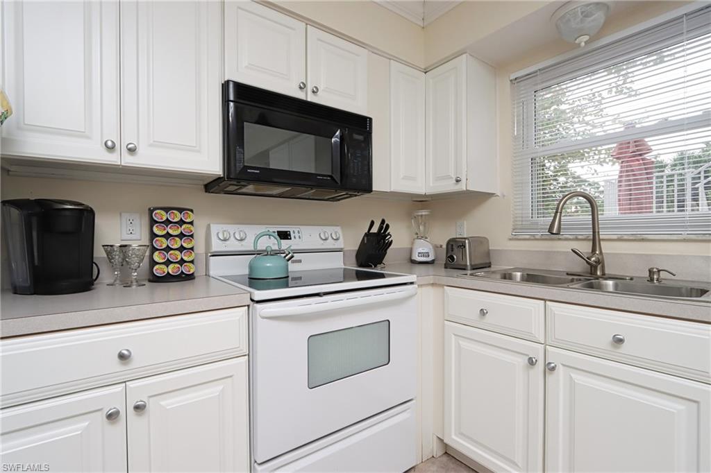 940 3rd Street South, Unit 101 Naples, FL 34102 - Photo 12 of 20 Kitchen featuring white electric range, white cabinets, black microwave, light countertops, and crown molding