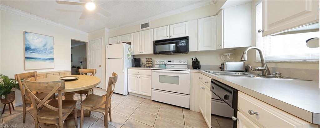 940 3rd Street South, Unit 101 Naples, FL 34102 - Photo 8 of 20 Kitchen with black appliances, crown molding, light tile patterned floors, light countertops, and white cabinetry