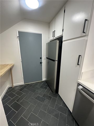 a view of a refrigerator in kitchen and an empty room with wooden floor