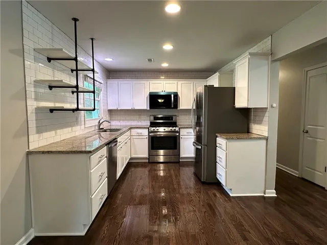 a kitchen with granite countertop a refrigerator a sink dishwasher a stove and a refrigerator with wooden floor