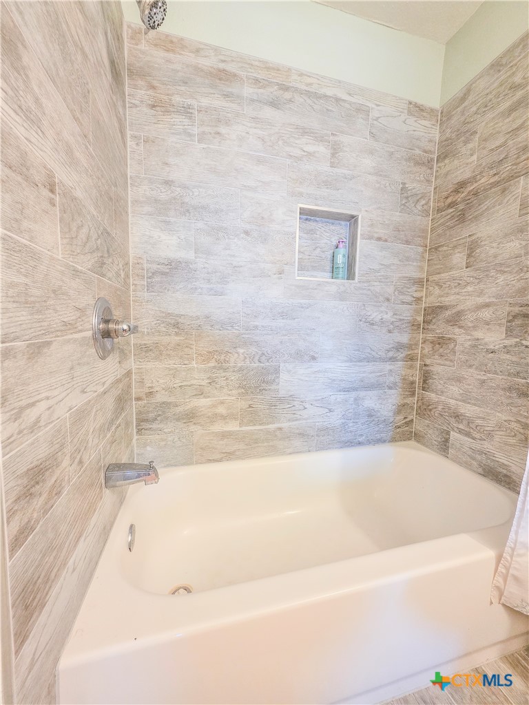 376 Haddock Drive Palacios, TX 77465 - Photo 19 of 41 This bathroom features a sleek bathtub with modern gray tile walls, offering a clean and stylish look. A built-in shelf provides convenient storage for toiletries.
