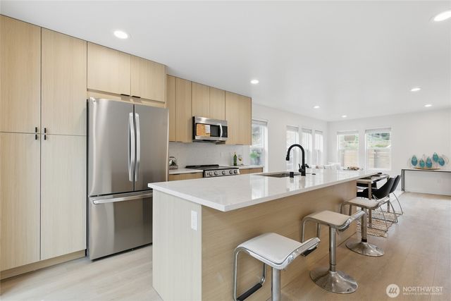 a kitchen with stainless steel appliances granite countertop a refrigerator a sink a stove and white cabinets with wooden floor